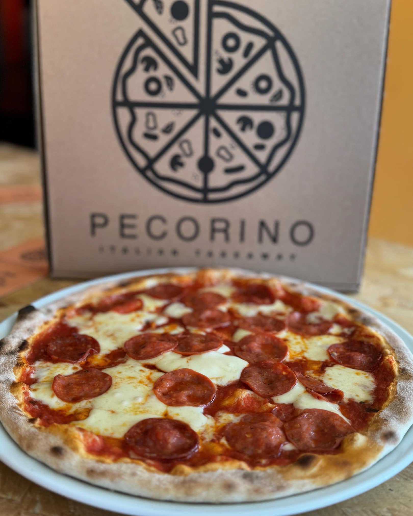 A freshly baked Salamino pizza served on a plate alongside a pizza box from Pecorino